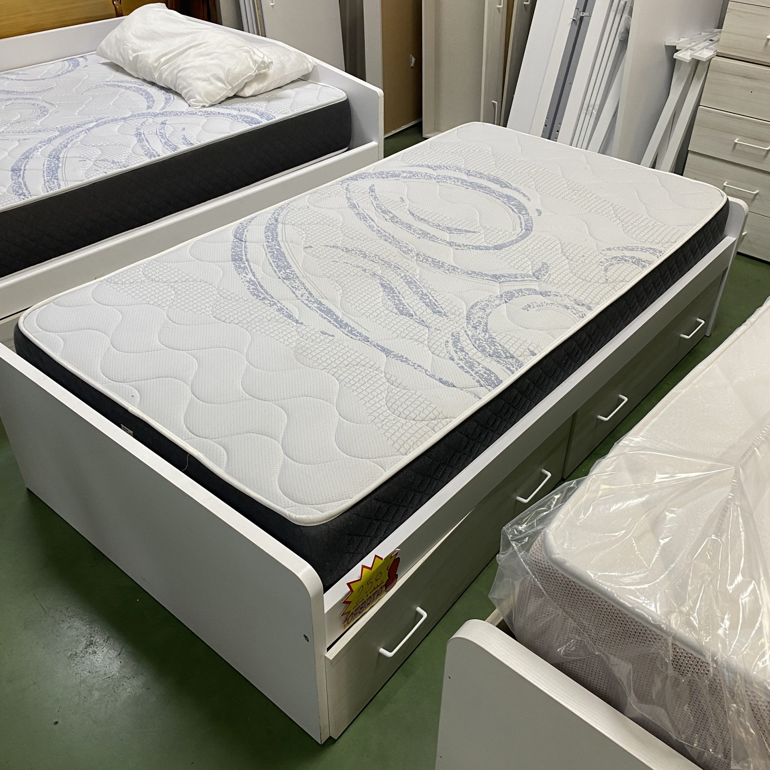 Cama individual blanca con canapé de almacenamiento y tres cajones laterales, colchón blanco con estampado azul y laterales negros,